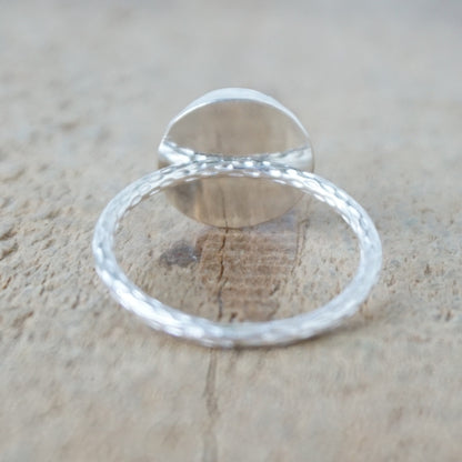 back view of A sterling silver ring featuring a round turquoise cabochon stone with natural dark veining, set against a neutral, textured beige background.