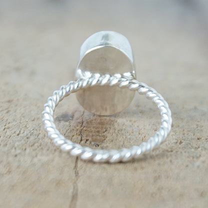 back view of A silver ring featuring an oval turquoise stone with natural matrix inclusions, set on a twisted rope-style silver band, on a wooden surface.