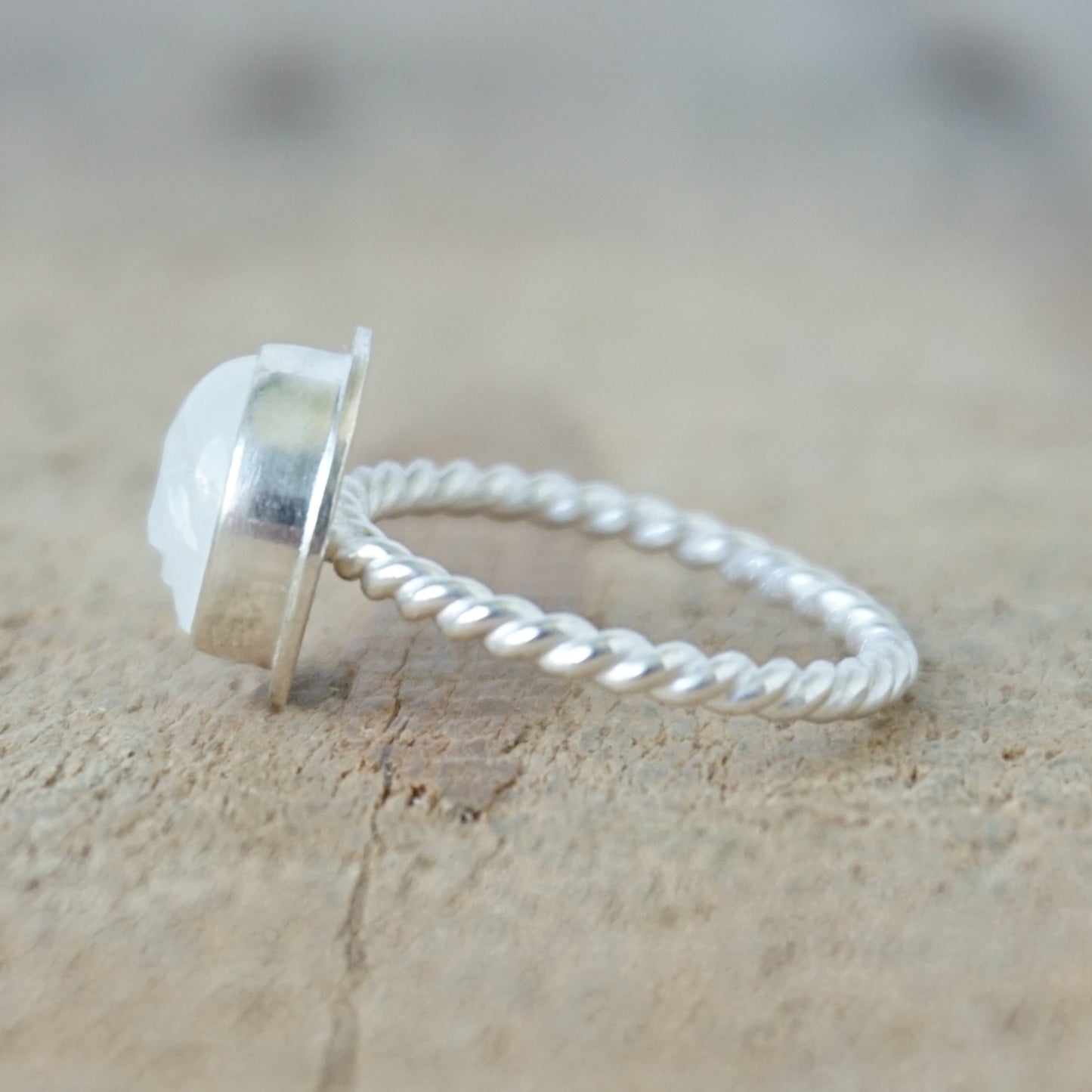 side view of A sterling silver ring featuring a round bezel-set white stone with a carved face, on a wooden surface.