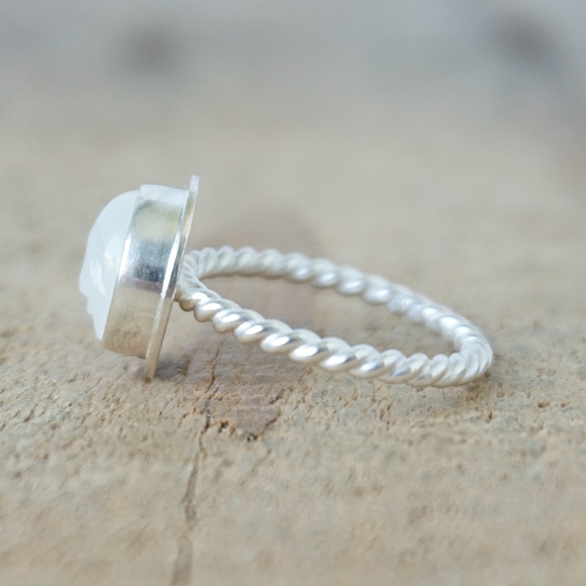 side view of A sterling silver ring featuring a round bezel-set white stone with a carved face, on a wooden surface.
