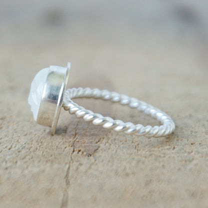side view of A sterling silver ring featuring a round bezel-set white stone with a carved face, on a wooden surface.