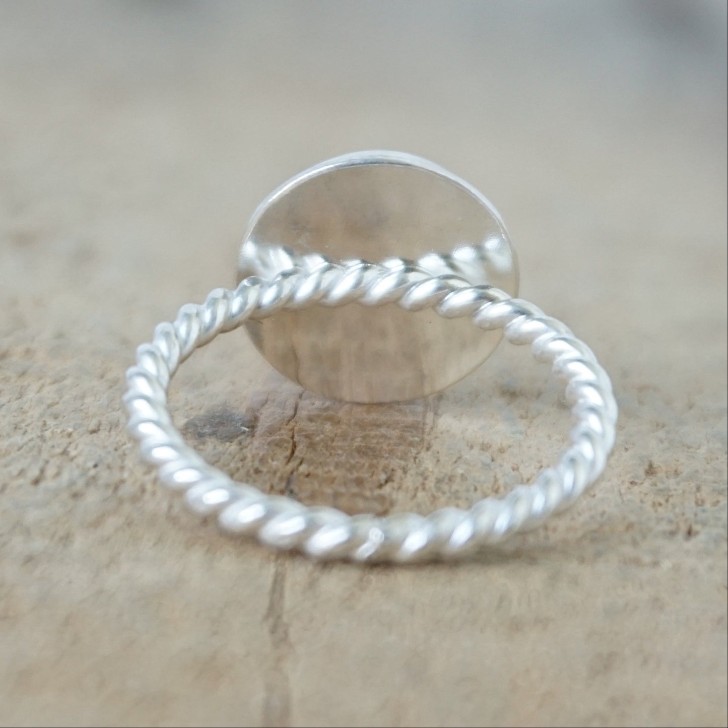 back view of A sterling silver ring featuring a round bezel-set white stone with a carved face, on a wooden surface.
