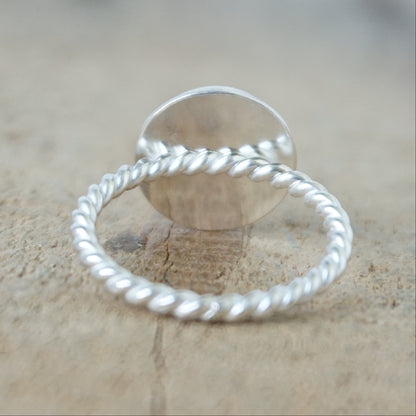 back view of A sterling silver ring featuring a round bezel-set white stone with a carved face, on a wooden surface.