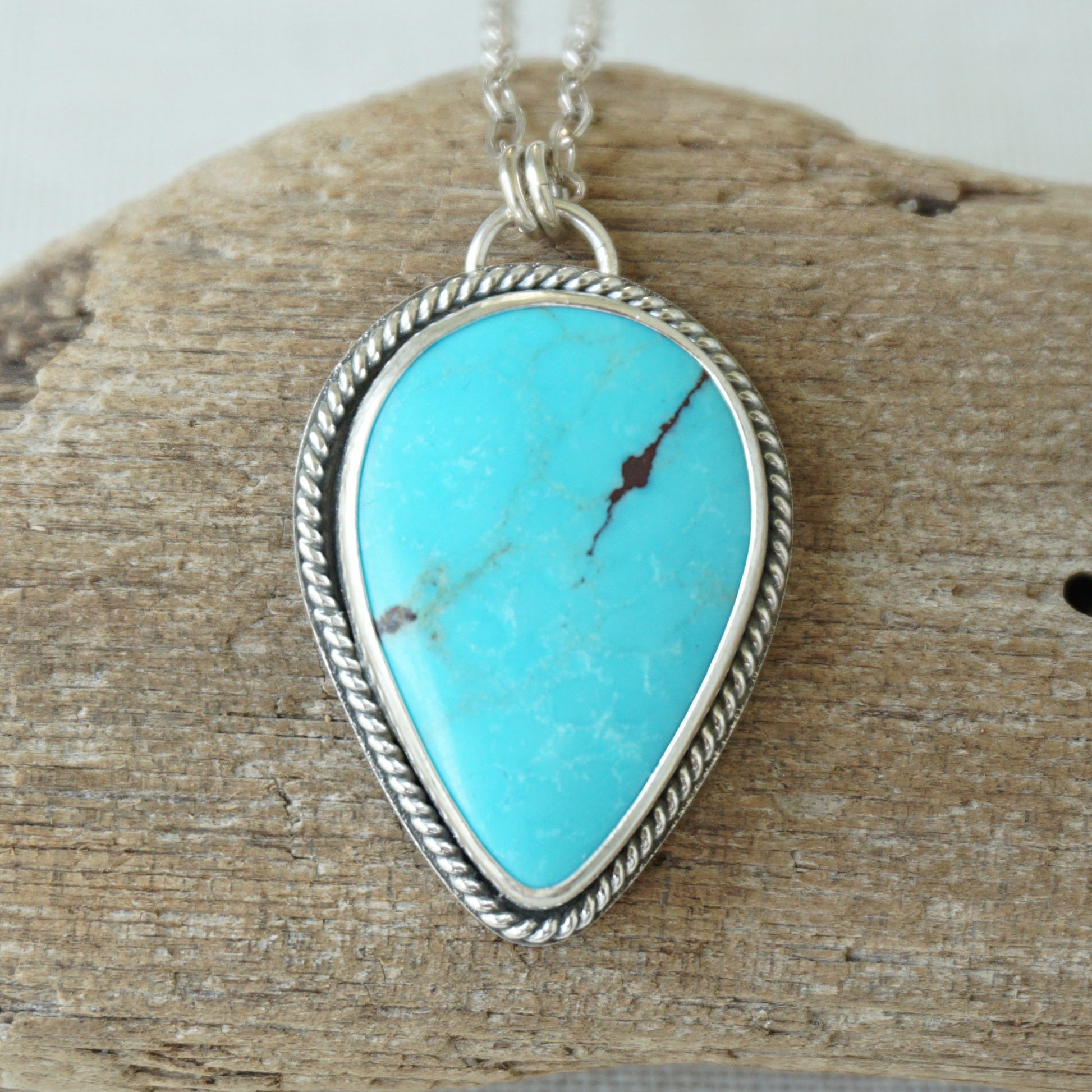 Sterling silver pendant with teardrop shaped turquoise stone, against a wooden background