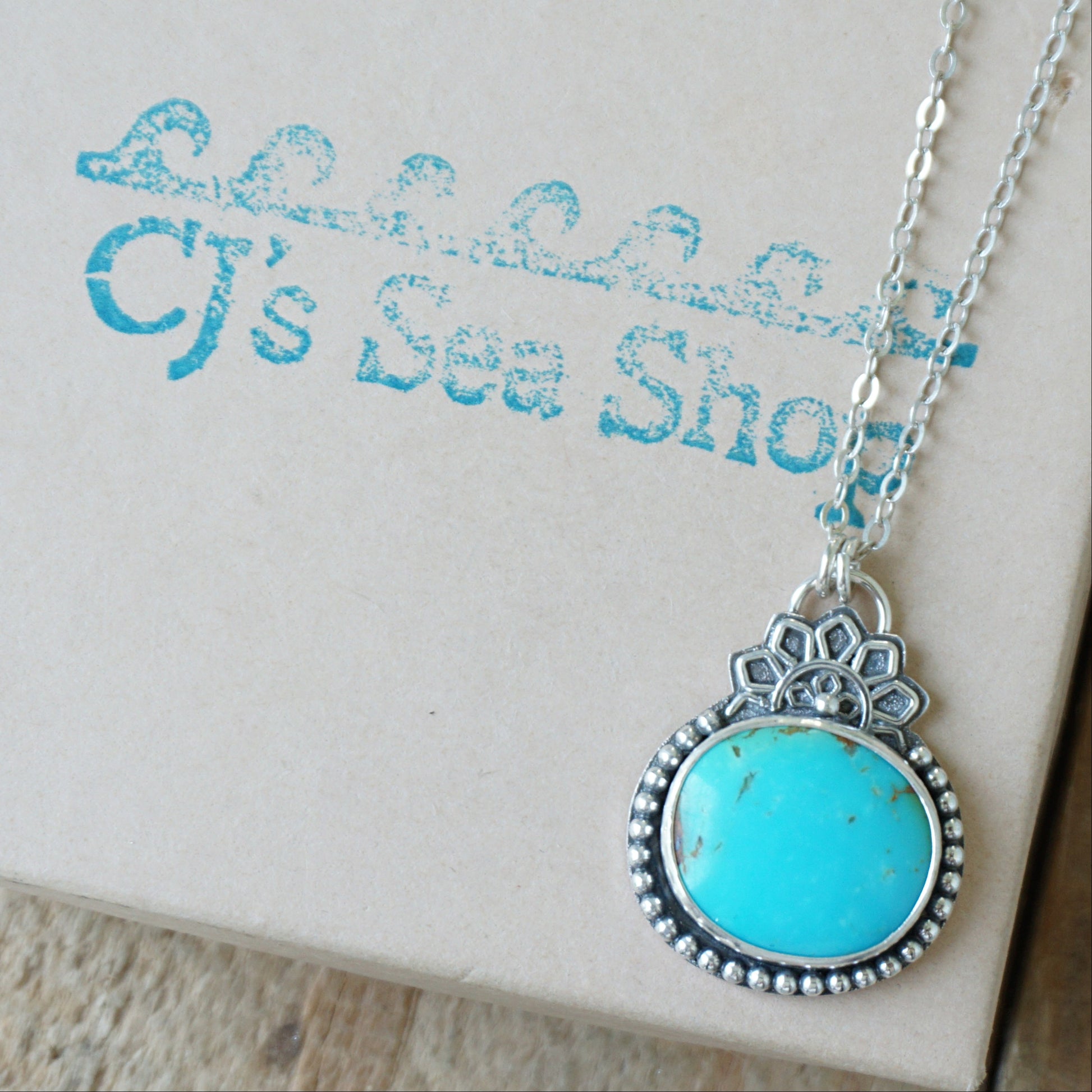 A turquoise pendant set in sterling silver with silver floral accents, displayed on a gift box