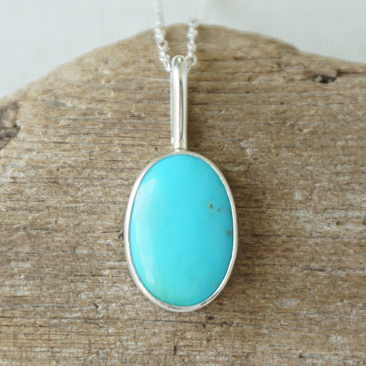 sterling silver pendant with turquoise stone, against a wooden background
