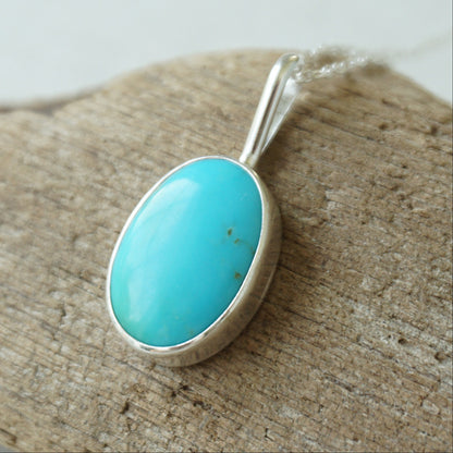 sterling silver pendant with turquoise stone, against a wooden background