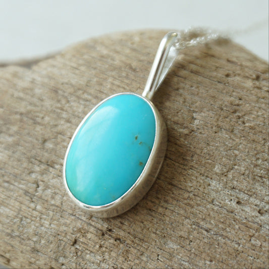sterling silver pendant with turquoise stone, against a wooden background