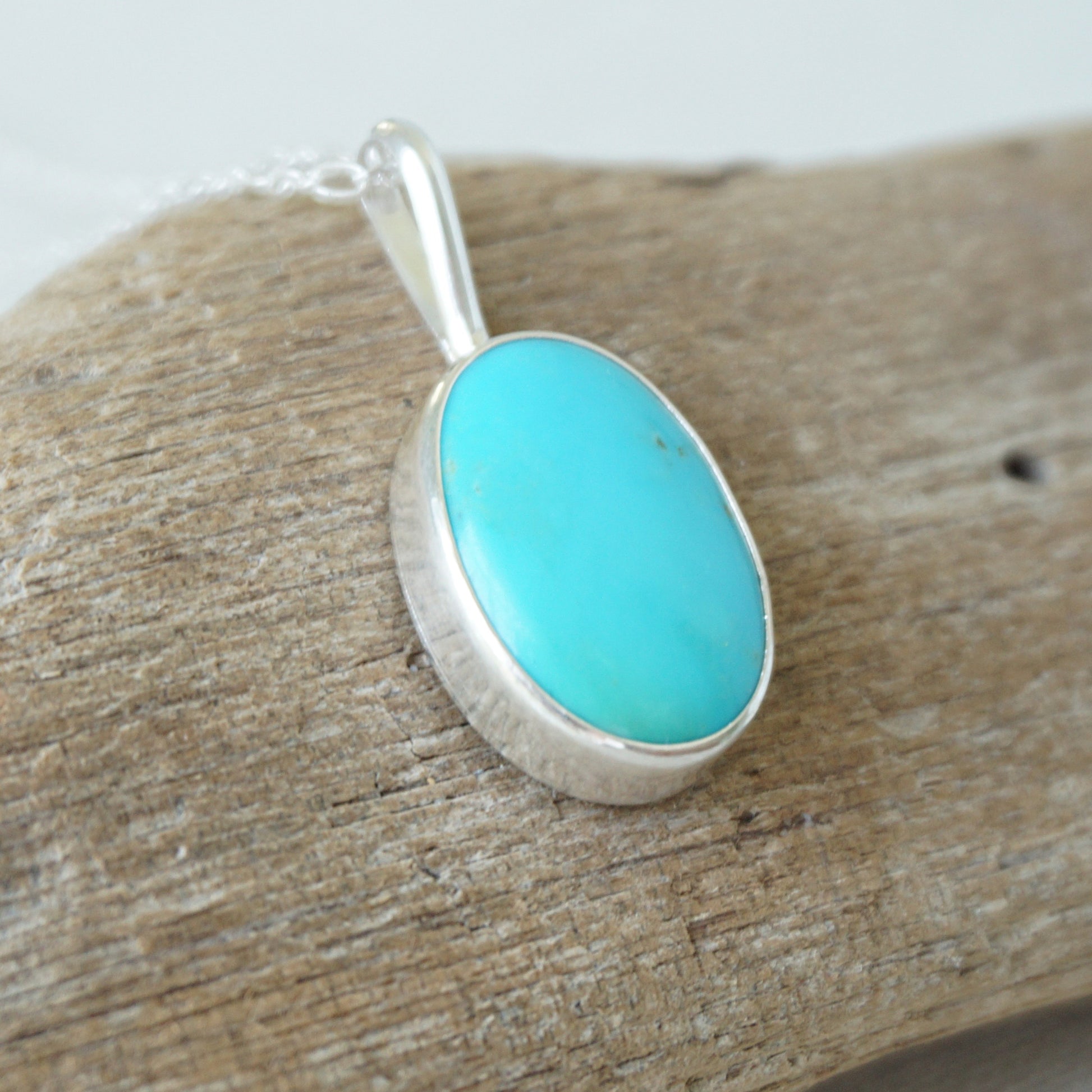 sterling silver pendant with turquoise stone, against a wooden background