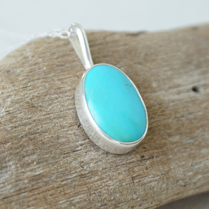 sterling silver pendant with turquoise stone, against a wooden background