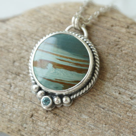 Sterling silver pendant with green and brown stone, against a wooden background