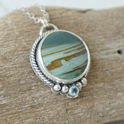 Sterling silver pendant with green and brown stone, against a wooden background