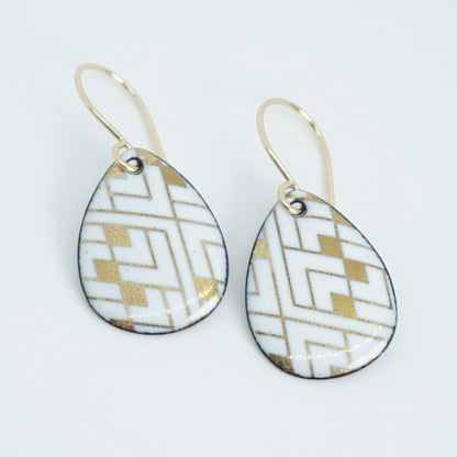 A pair of teardrop-shaped drop earrings with a white and gold geometric pattern, suspended from gold fishhook wires on a white background.