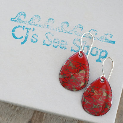 Teardrop shaped, red enamel earrings with gold geometric designs, displayed on a gift box