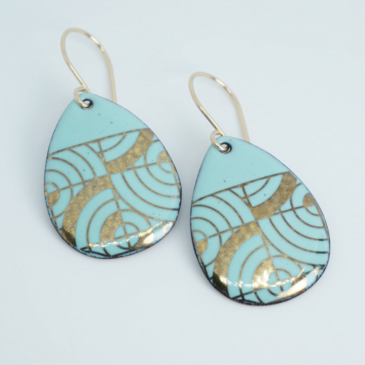 Teardrop shaped, seafoam green enamel earrings with gold geometric designs, against a white background