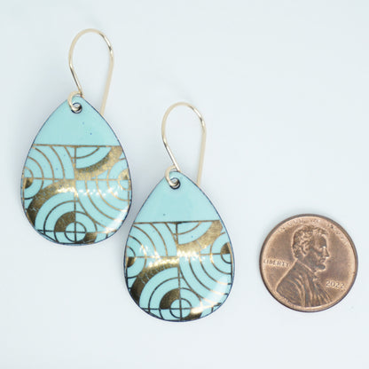 Teardrop shaped, seafoam green enamel earrings with gold geometric designs, next to a penny for scale, against a white background