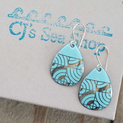 Teardrop shaped, seafoam green enamel earrings with gold geometric designs, displayed on a gift box