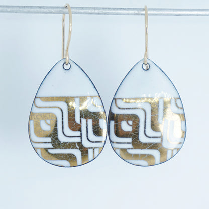 Teardrop shaped, white enamel earrings with gold geometric designs, against a white background