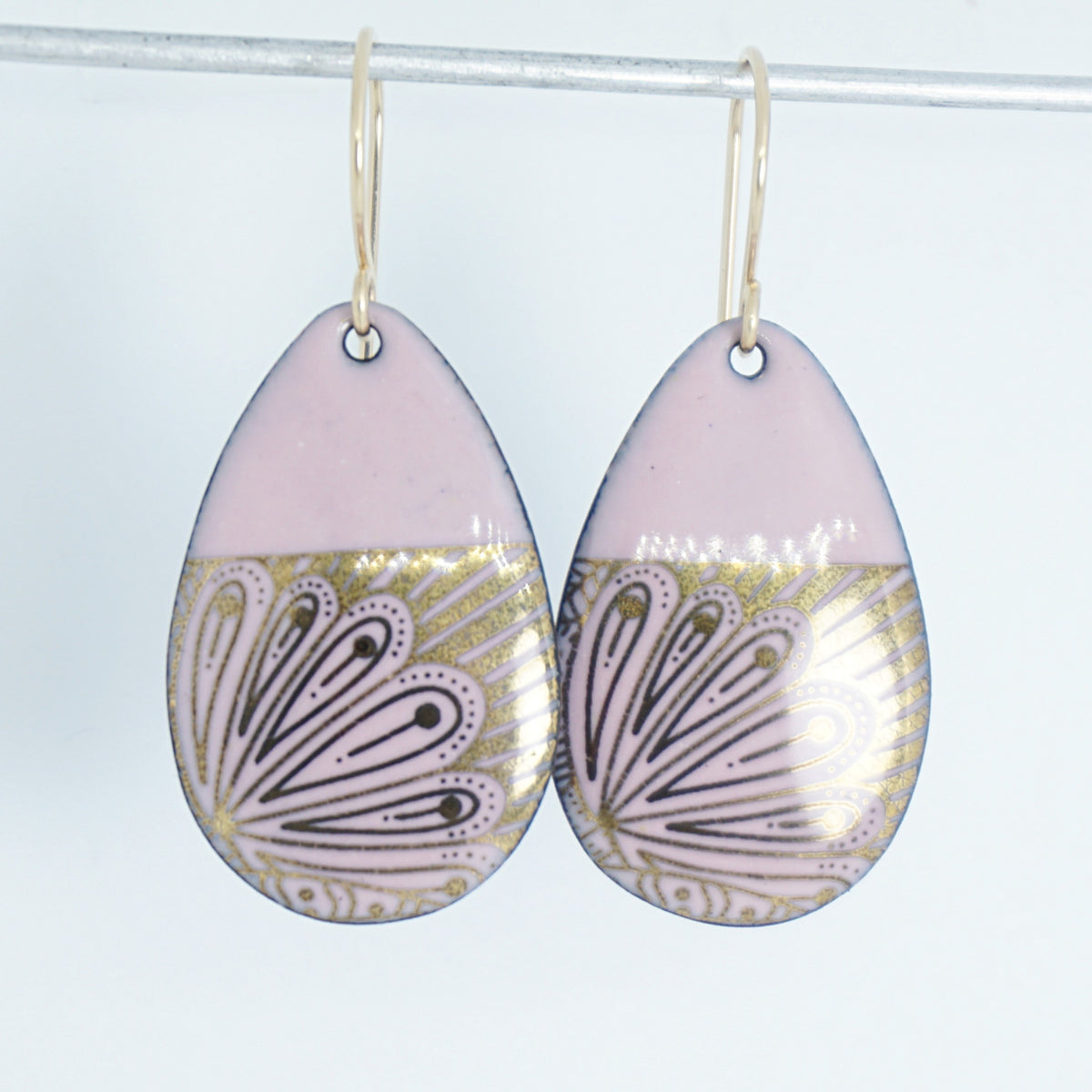 Teardrop shaped, pink enamel earrings with gold floral designs, against a white background