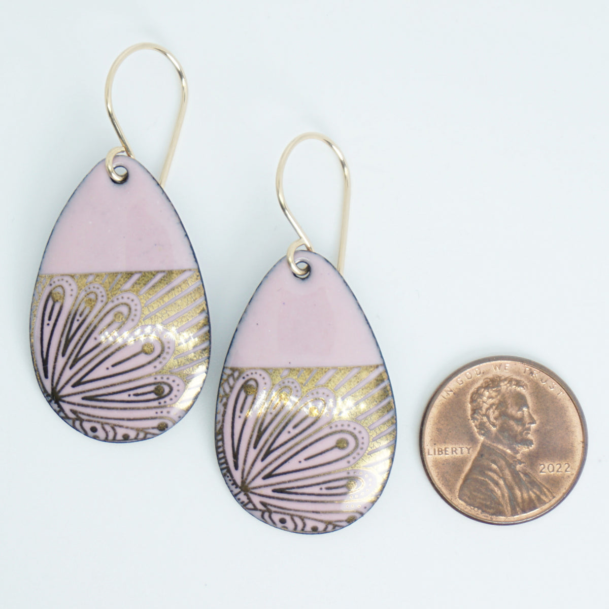 Teardrop shaped, pink enamel earrings with gold floral designs, next to a penny for scale, against a white background