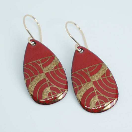 Teardrop shaped red enamel earrings with gold geometric design, against a white background