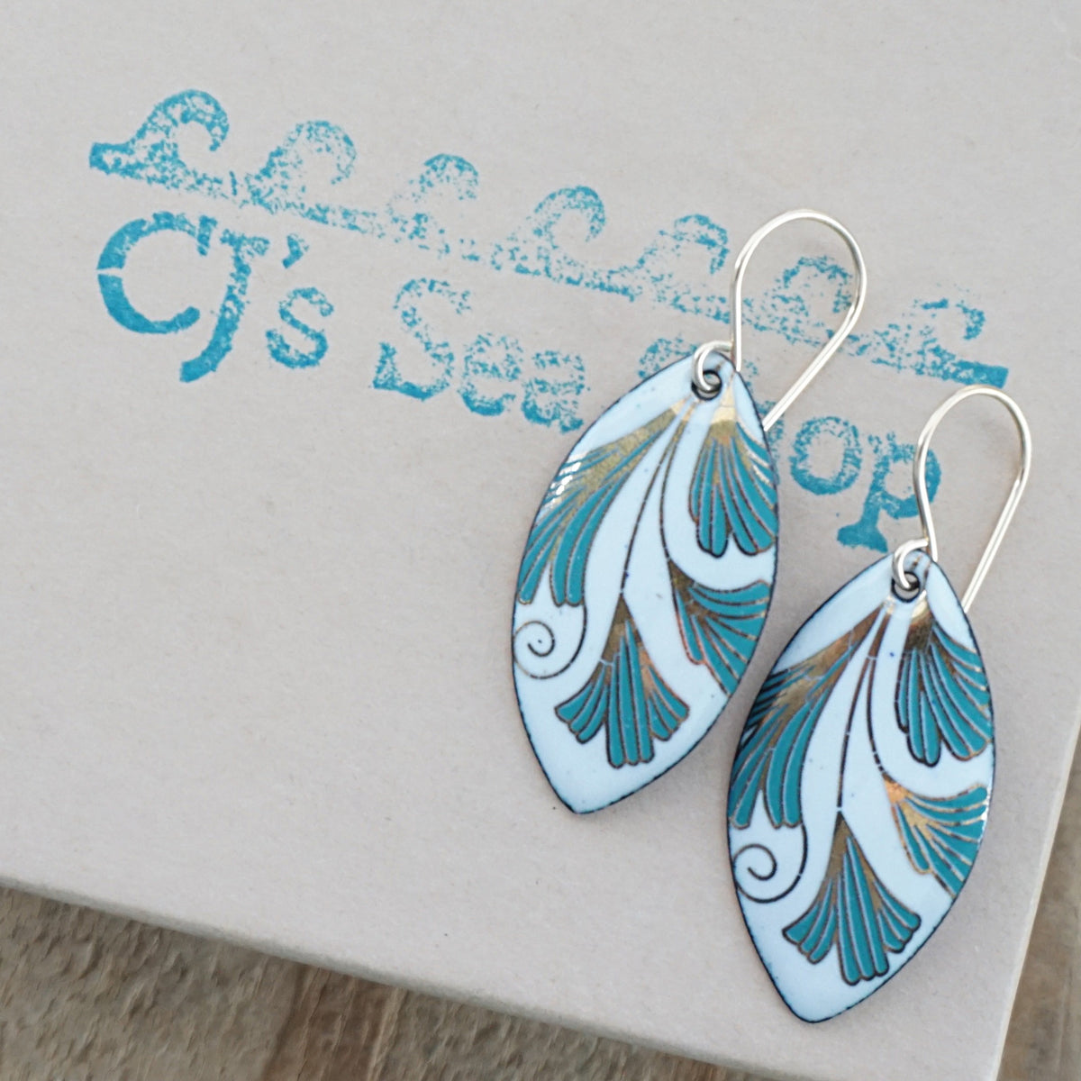 Marquis shaped enamel earrings with green and gold leaves, displayed on a gift box