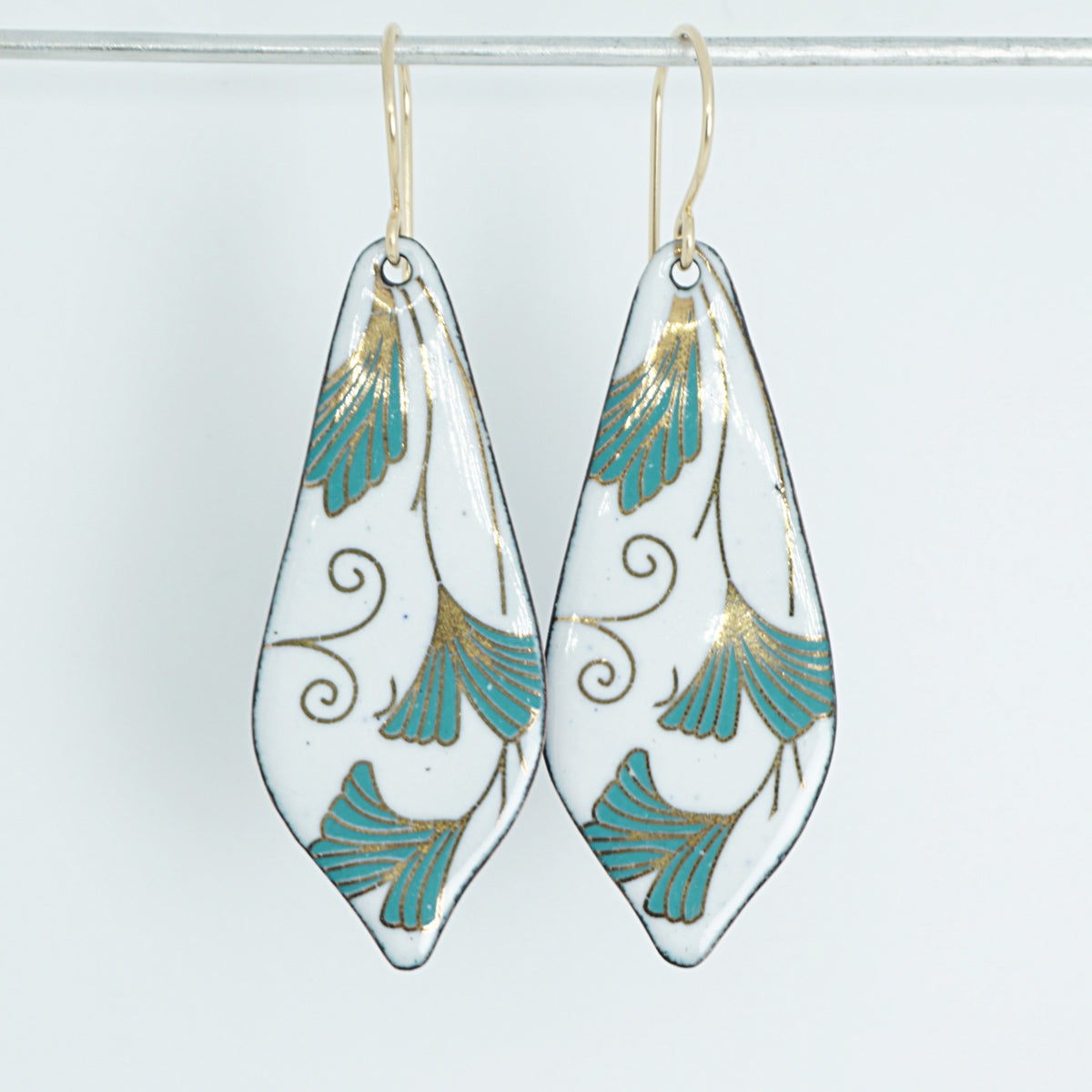 Teardrop shaped enamel earrings with green and gold leaves, against a white background