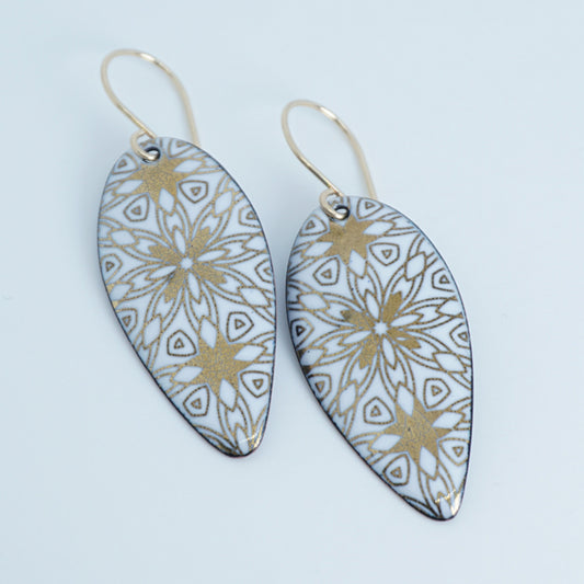 a pair of white enamel earrings with gold designs, against a white background