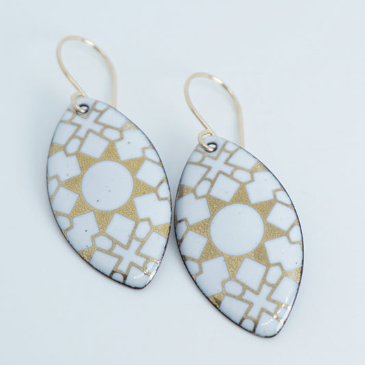 a pair of white enamel earrings with gold designs, against a white background