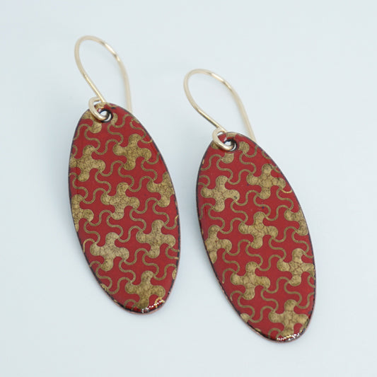 a pair of red enamel earrings with gold designs, against a white background