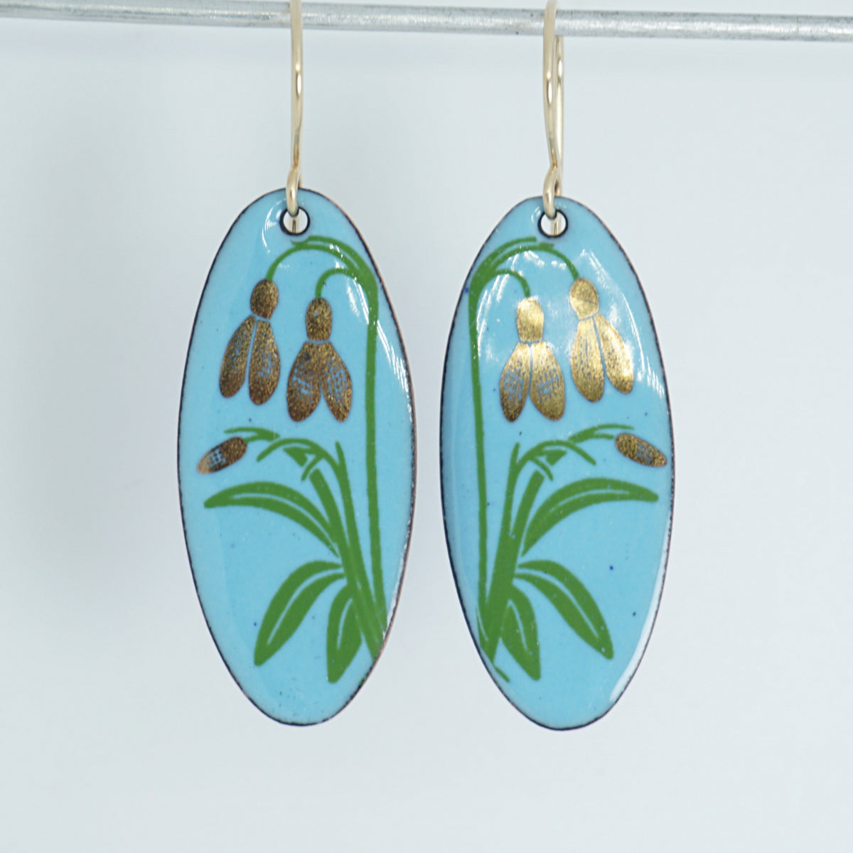 a pair of light blue enamel oval shaped earrings with gold flower accents, against a white background