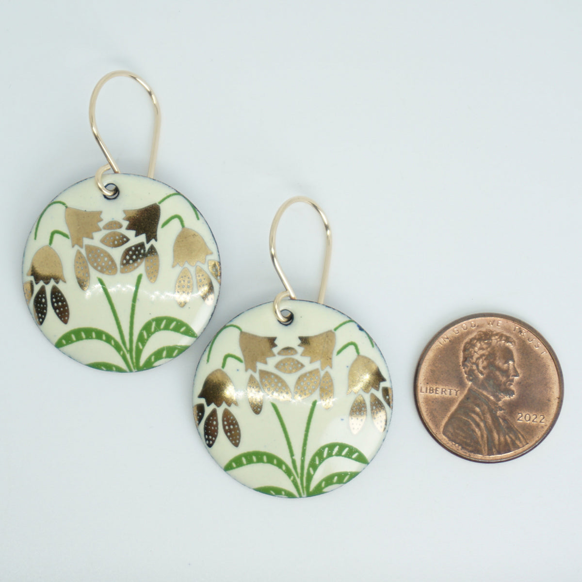 a pair of yellow enamel disc shaped earrings with gold flower accents, next to a penny for scale, against a white background
