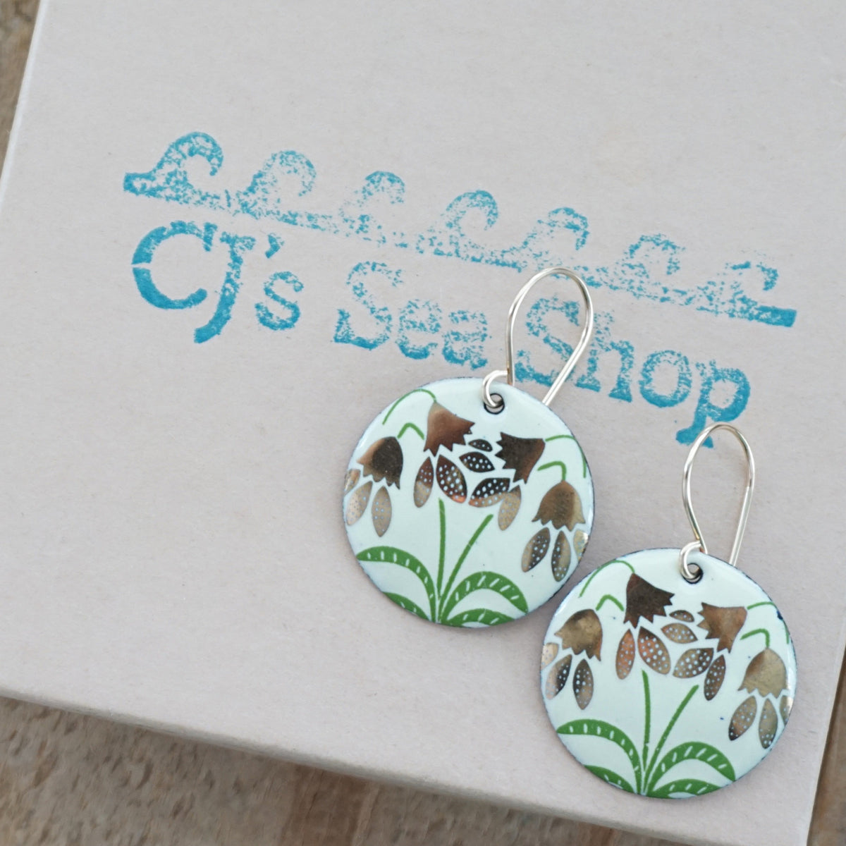 a pair of yellow enamel disc shaped earrings with gold flower accents, displayed on a gift box