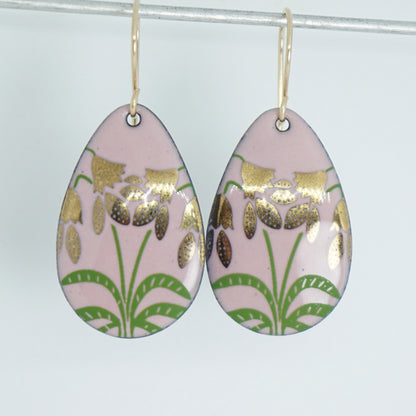 a pair of pink enamel teardrop shaped earrings with gold flower accents, against a white background