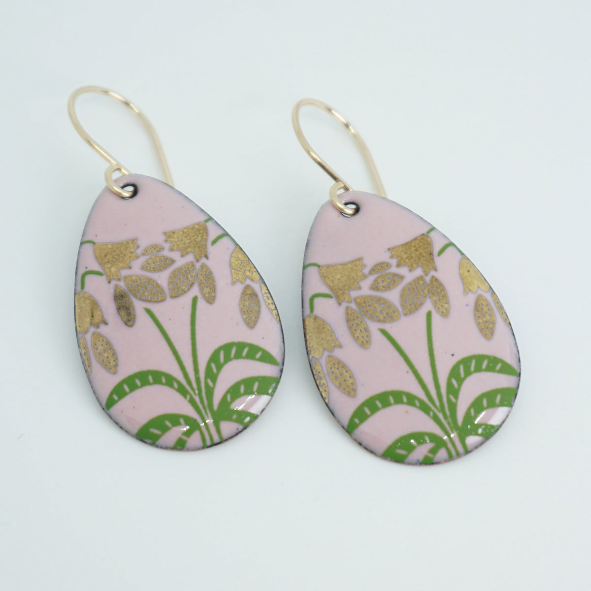 a pair of pink enamel teardrop shaped earrings with gold flower accents, against a white background