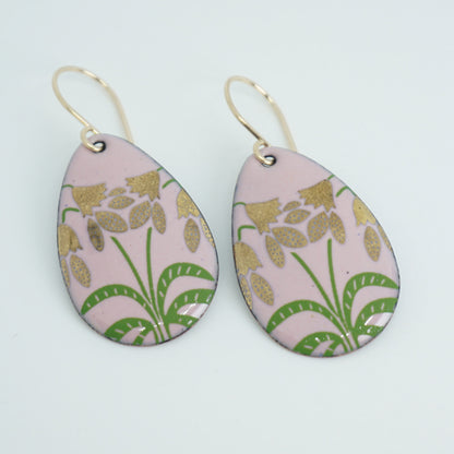 a pair of pink enamel teardrop shaped earrings with gold flower accents, against a white background