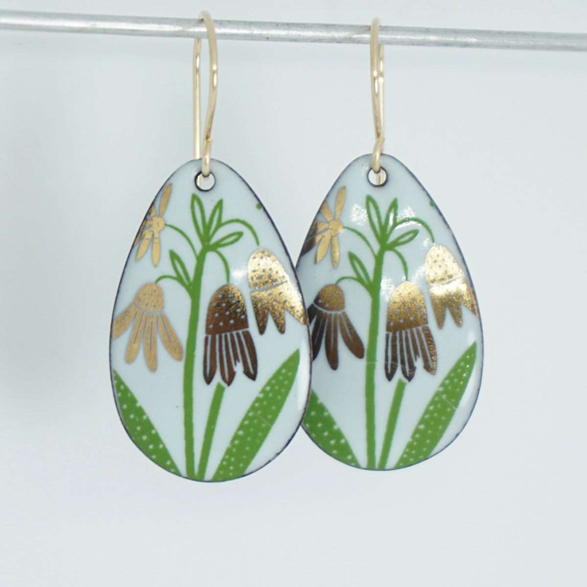 a pair of seafoam green enamel teardrop shaped earrings with gold flower accents, against a white background