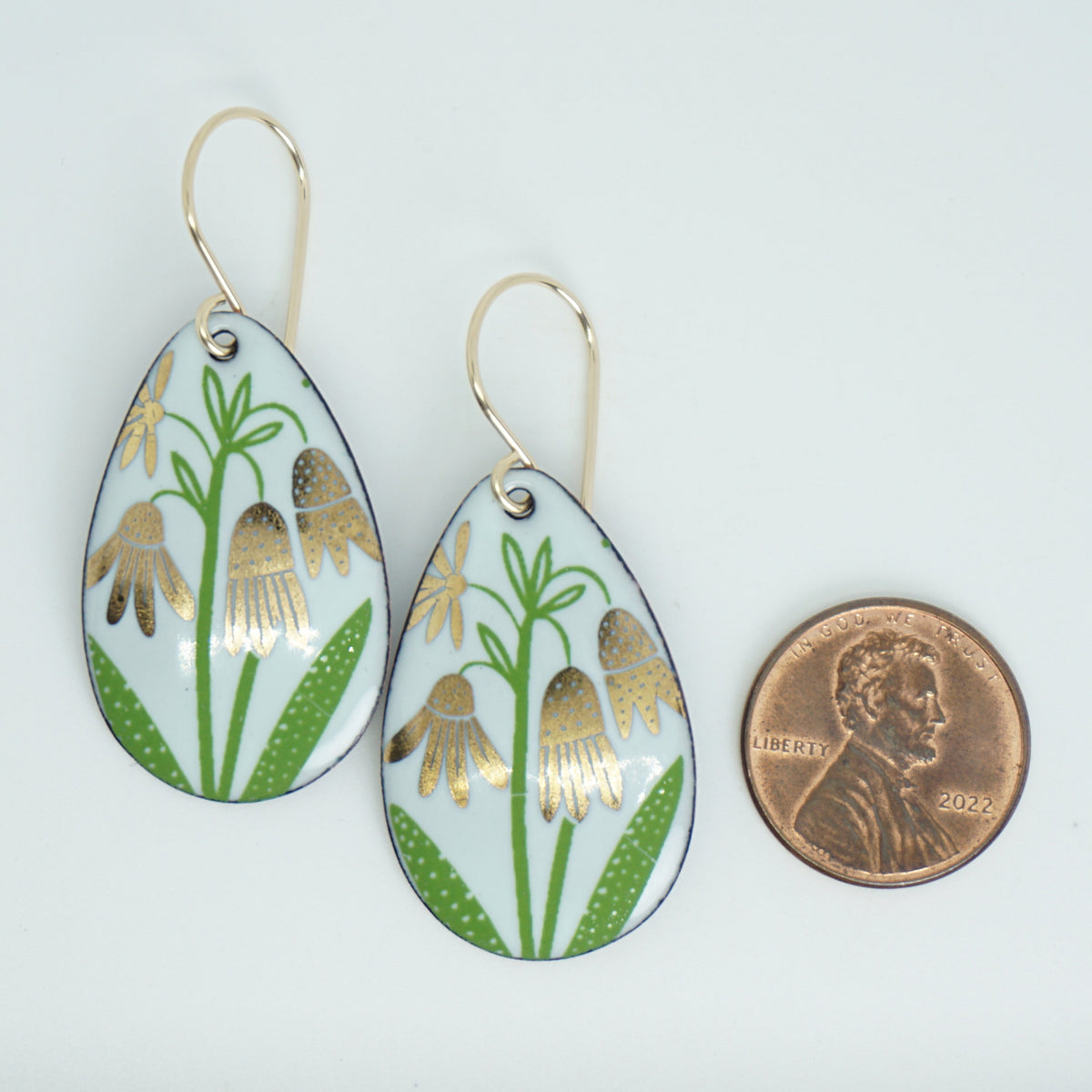 a pair of seafoam green enamel teardrop shaped earrings with gold flower accents,  next to a penny for scale, against a white background