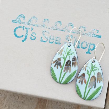 a pair of seafoam green enamel teardrop shaped earrings with gold flower accents, displayed on a gift box