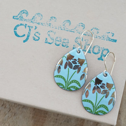 a pair of light blue enamel teardrop shaped earrings with gold flower accents, displayed on a gift box