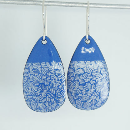a pair of blue enamel teardrop shaped earrings with white accents, against a white background