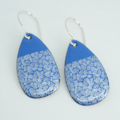 a pair of blue enamel teardrop shaped earrings with white accents, against a white background