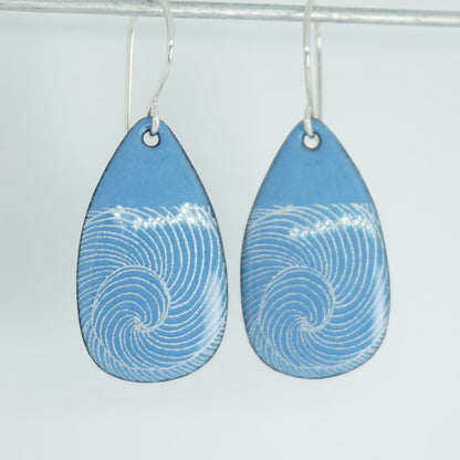 a pair of blue enamel teardrop shaped earrings with white wave accents, against a white background