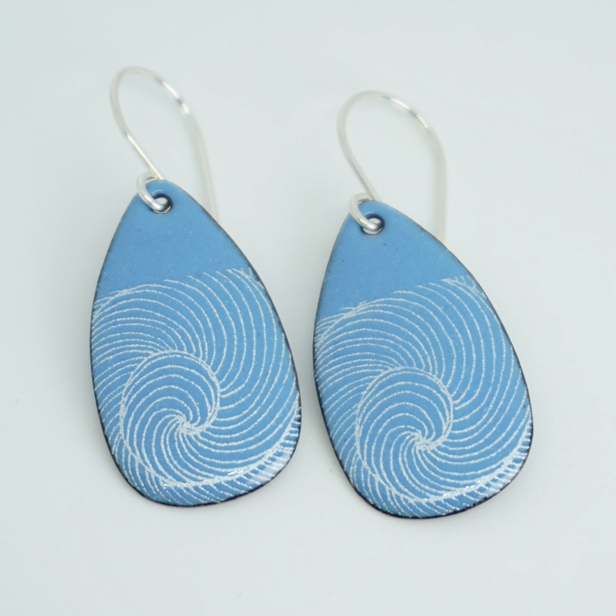 a pair of blue enamel teardrop shaped earrings with white wave accents, against a white background
