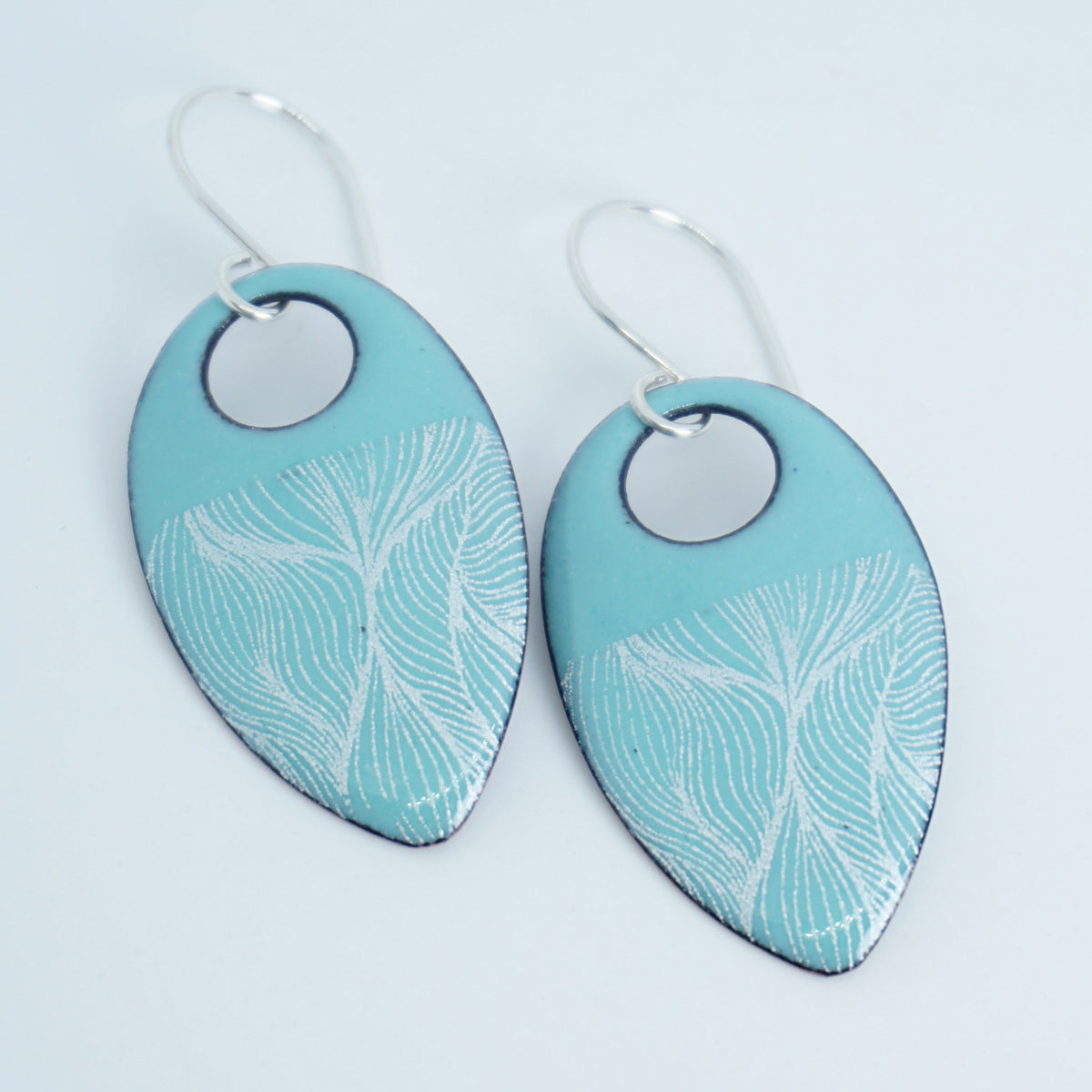a pair of light green enamel teardrop shaped earrings with white feathery accents, against a white background