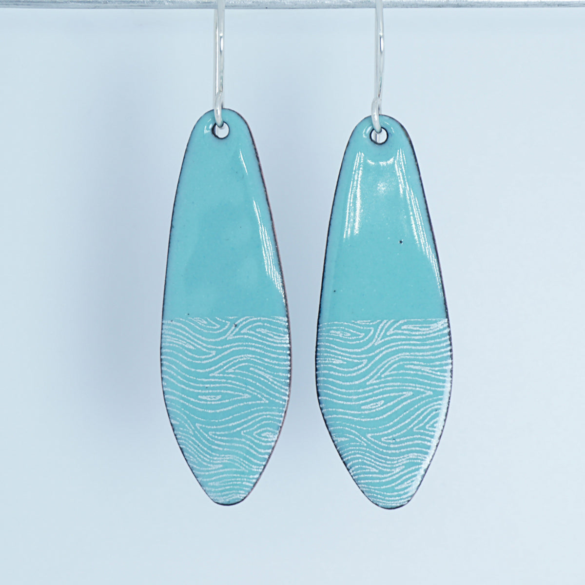 a pair of light green enamel teardrop shaped earrings with white wavy accents, against a white background