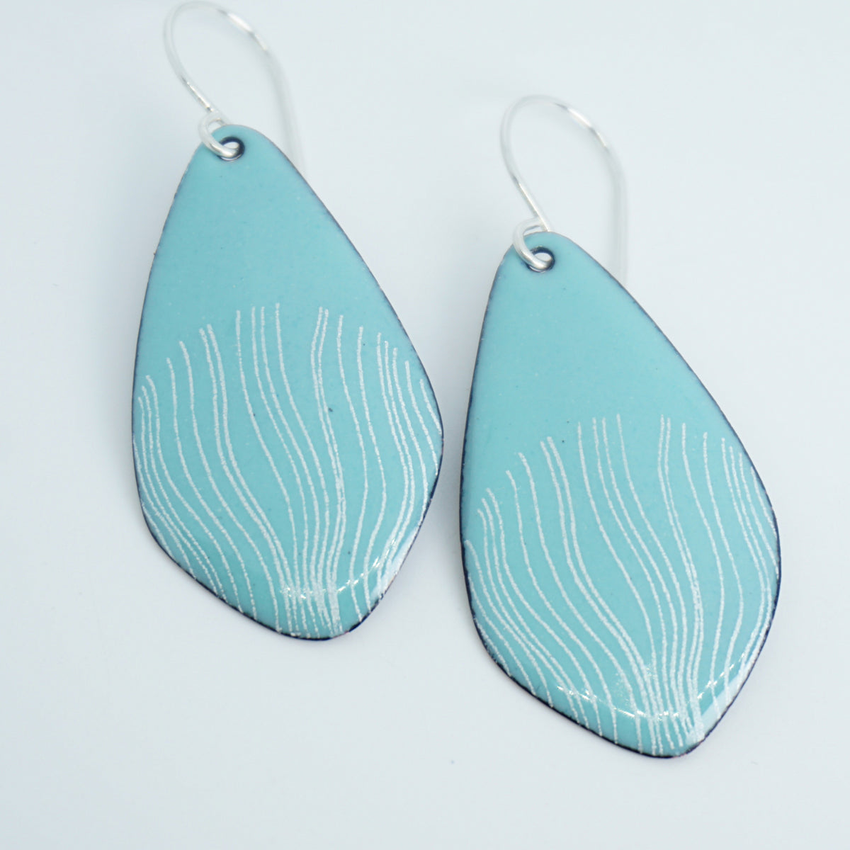 a pair of light green enamel teardrop shaped earrings with white wavy accents, against a white background