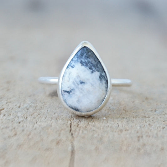 silver ring with a white and dark grey stone, against a wooden background