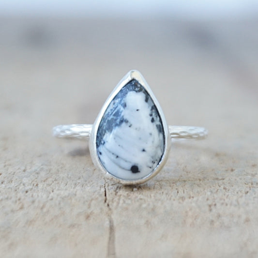 silver ring with a white and dark grey stone, against a wooden background