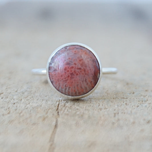 silver ring with a round reddish stone, against a wooden background
